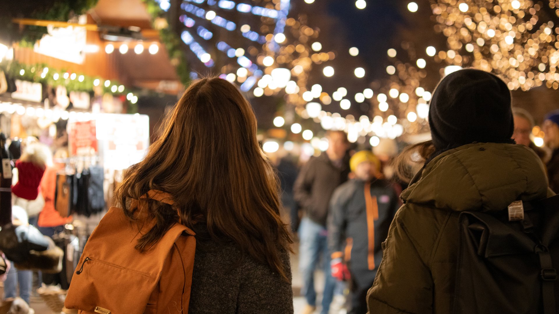Two people walking through a lit-up market in Oslo.
