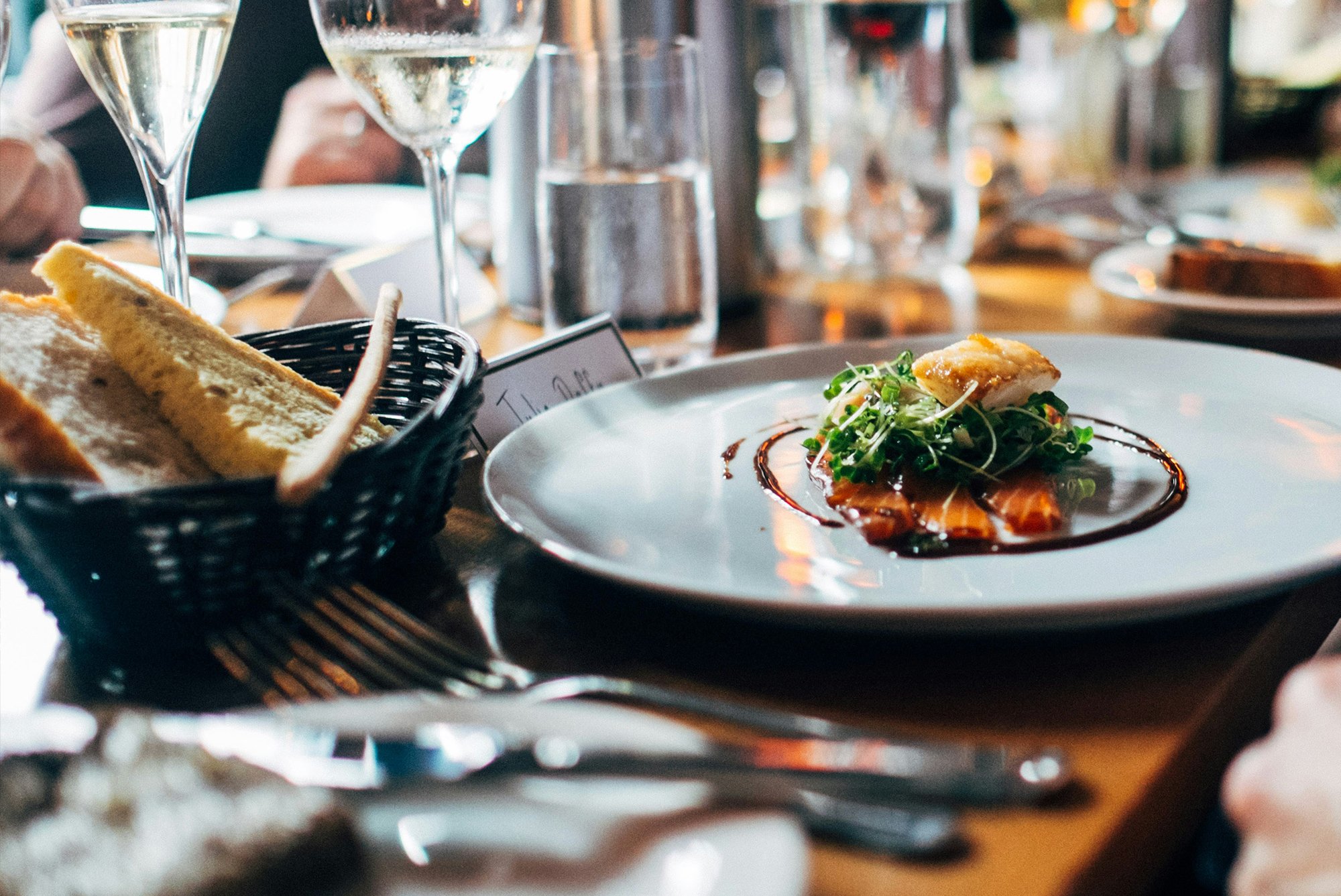 Dining table with gourmet dish, wine glasses, and breadsticks at a formal restaurant setting.
