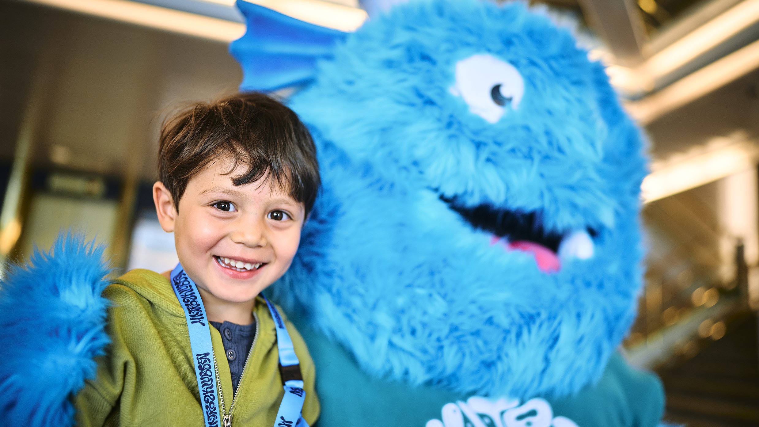 Person standing next to a large blue furry mascot with white eyes and a big smile in the Matrosklubben.