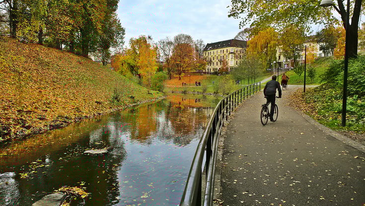 Person riding a bicycle on a path next to a river in autumn.