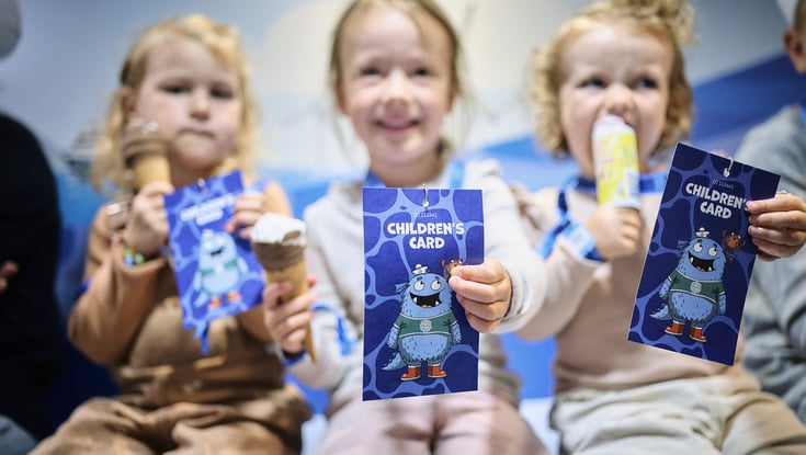hree children holding up "Children's Card" booklets featuring a cartoon character in the Matrosklubben.