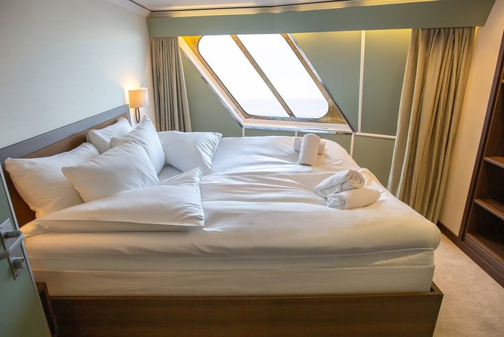 Cabin with a neatly made bed, window, and towel swans.