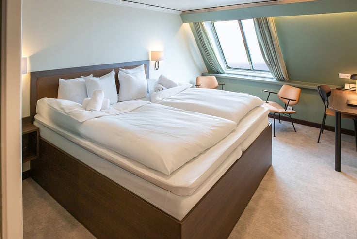 Modern cabin on the ship with a large bed, two chairs, and a desk.