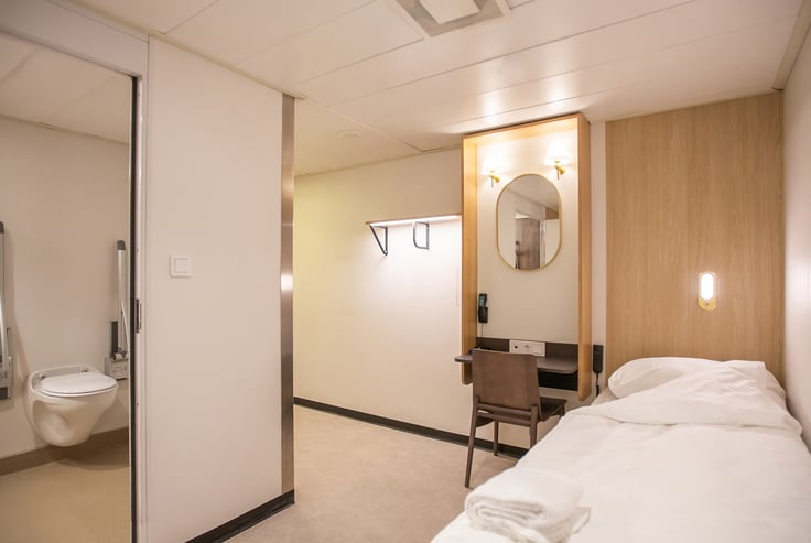Accessible cabin with a bed, desk, and bathroom.