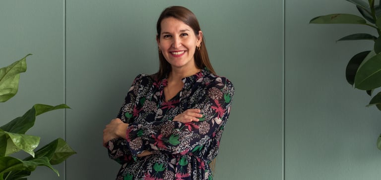 Smiling woman standing with arms crossed in front of a green wall.