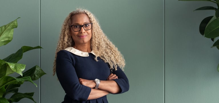 Woman with curly hair standing with arms crossed in front of a green wall.