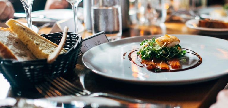 Dining table with gourmet dish, wine glasses, and breadsticks at a formal restaurant setting.