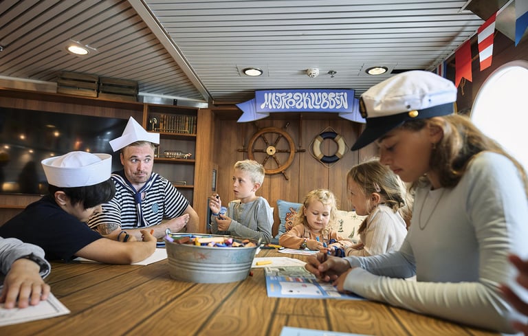 Group of people, including children and adults, engaged in an activity with paper and markers in the Matrosklubben.